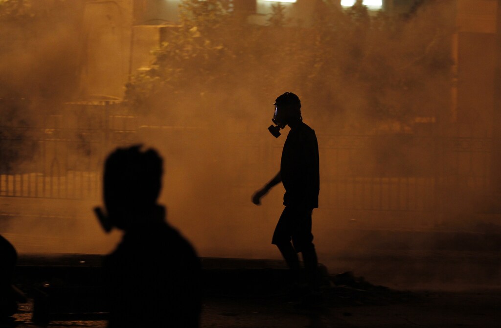 A protester wearing a gas mask takes cover from tear gas fired by riot police during clashes in the village of Bilad al-Qadeem, south of Manama, July 19, 2013. Bahrain's Ministry of Interior rejected permission for the weekly anti-government rally organized by Bahrain's main opposition party Al Wefaq. Protesters from various villages defied the ban as they took to the streets demanding the government give them more rights. REUTERS/Hamad I Mohammed (BAHRAIN - Tags: POLITICS CIVIL UNREST) - GM1E97K0JD201