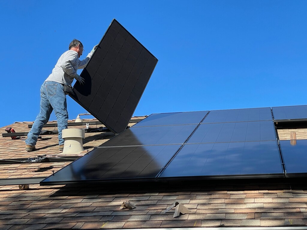 Un trabajador instala paneles solares en el tejado de una casa.