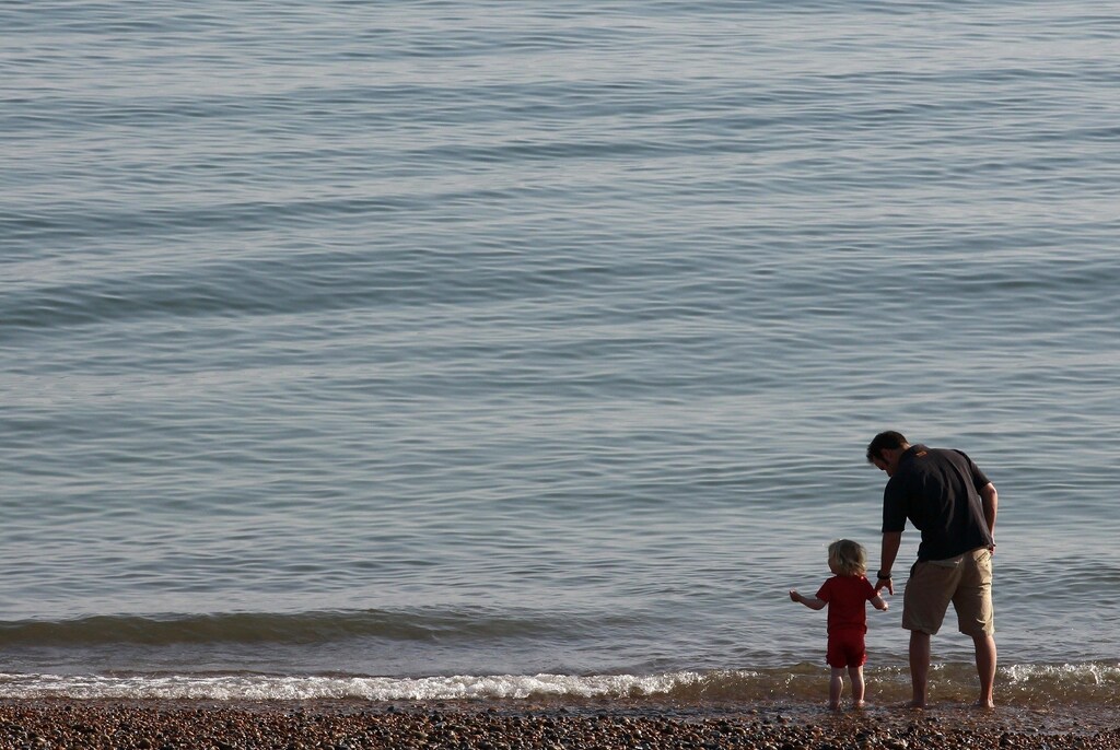 A man and child walk by the sea in Brighton, southern England April 20, 2011. The unseasonably hot April weather follows the UK's driest March for 60 years, according to the Met Office. REUTERS/Luke MacGregor (BRITAIN - Tags: ENVIRONMENT TRAVEL SOCIETY) - RTR2LFYW