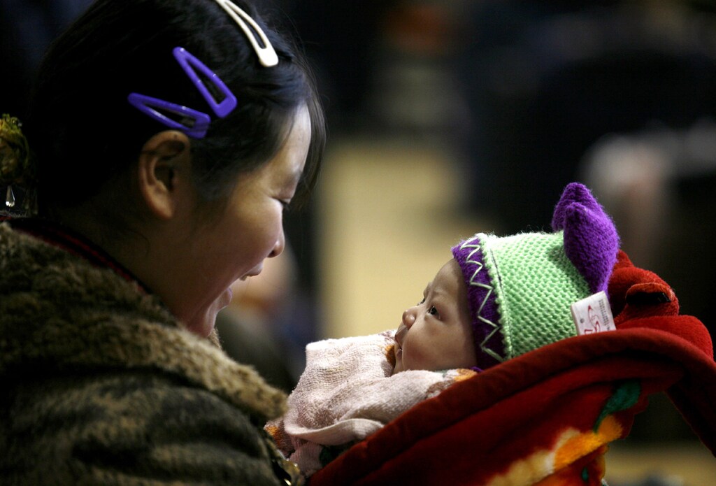 A mother smiles at her baby as they wait to board a train at a railway station in Hangzhou, eastern China's Zhejiang province January 23, 2007.
