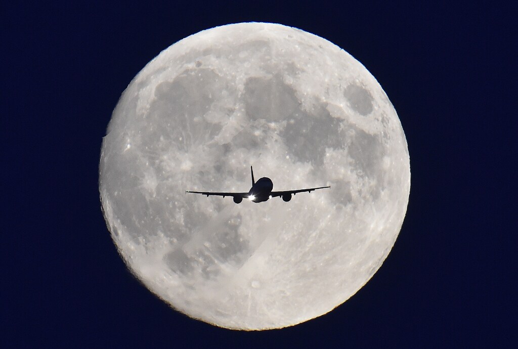 A passenger plane passes in front of the full moon as it makes a final landing approach to Heathrow Airport in west London, October 7, 2014. Heathrow Airport Holdings (HAH) is set to sell three British airports for 1 billion pounds ($1.6 billion) to a group including Spanish infrastructure firm Ferrovial, Singapore sovereign fund GIC and Australian bank Macquarie, according to Sky News. The sale of the three regional airports would leave HAH with just Heathrow, the west London hub that ranks as Britain's busiest and the world's third busiest airport. HAH would then be free to focus on its plan to gain government approval to build a third runway at Heathrow, an issue which has been at the centre of a long-running political tussle. REUTERS/Toby Melville (BRITAIN - Tags: BUSINESS TRANSPORT) - GM1EAA80BCJ01