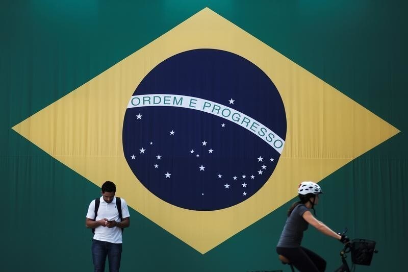 A man checks his mobile phone as a woman riding a bike passes next to a big Brazilian flag in Sao Paulo, Brazil June 28, 2018. REUTERS/Nacho Doce - RC1B7C56CC50