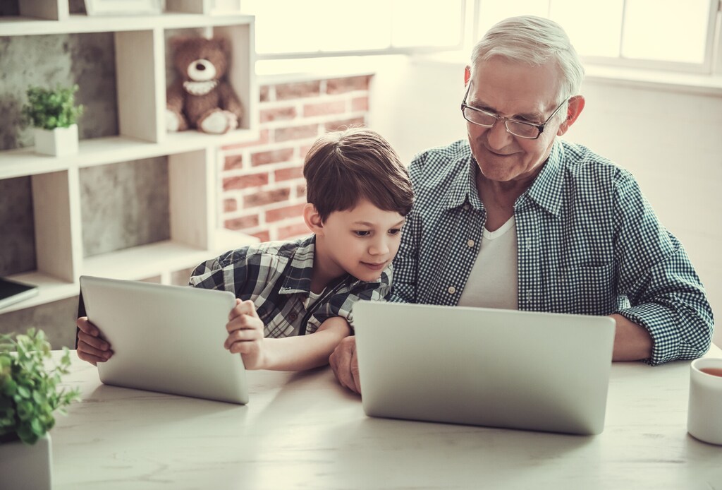 Grandfather and grandson using gadgets and smiling while spending time together at home; older workers; ageing well