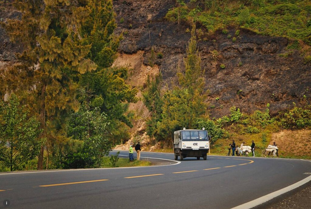 An electric OX truck drives past cyclists carrying heavy loads in Nyamasheke, Rwanda. September 14, 2021.