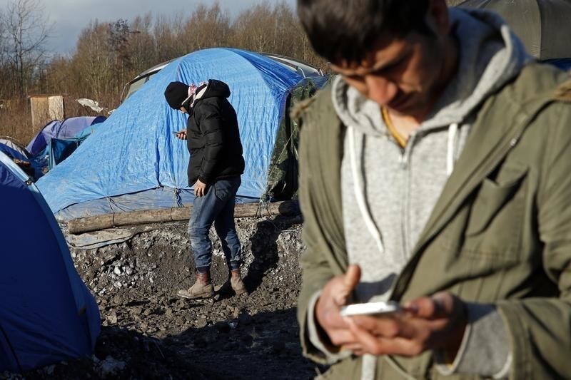 Migrants check their mobile phones next to shelters in a muddy field called the Grande-Synthe jungle, near Dunkirk, northern France, January 12, 2016. The Grande-Synthe jungle is a camp of tents and makeshift shelters where migrants and asylum seekers from Irak, Kurdistan and Syria gather. REUTERS/Benoit Tessier - LR2EC1C16N29E