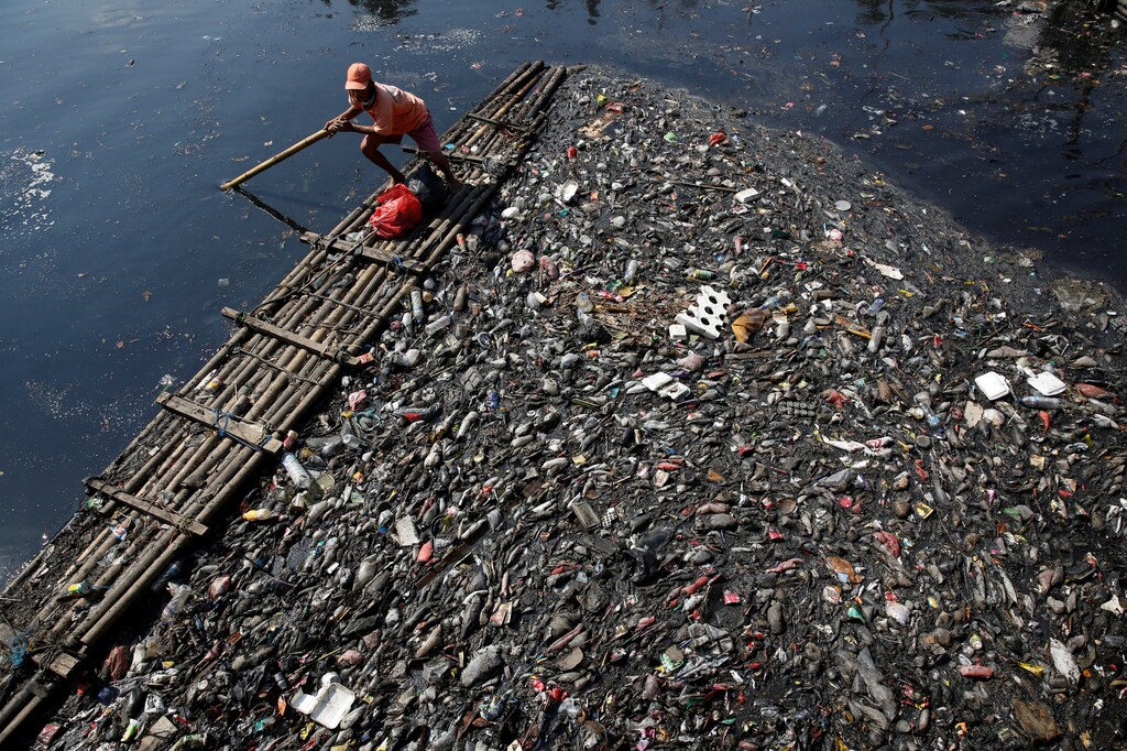 A government worker uses a raft to gather plastic and other debris for collection and disposal from the Sekretaris River in Jakarta, Indonesia, June 7, 2017. REUTERS/Darren Whiteside - RC1EEDDE11C0