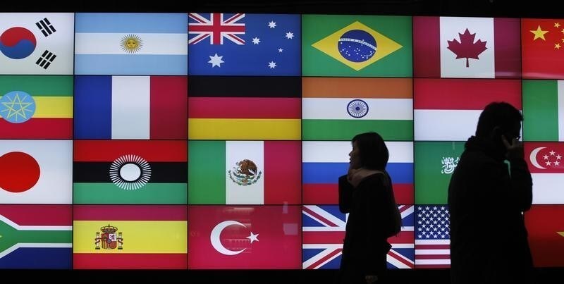 People using their mobile phones walk past a screen showing flags of the participating countries in the upcoming G20 summit in Seoul November 5, 2010. China on Friday pushed back strongly against U.S. policies ahead of a G20 summit, ridiculing Washington's plan to set current account targets and warning of risks in the Fed's monetary easing. REUTERS/Jo Yong-Hak (SOUTH KOREA - Tags: POLITICS BUSINESS) - GM1E6B51B3X01