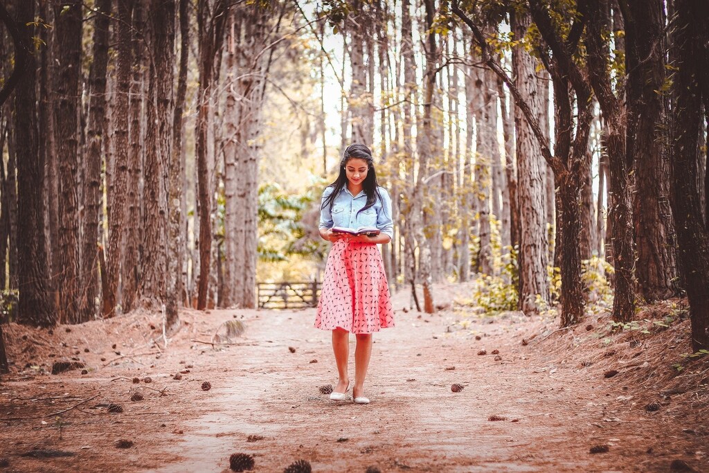 Woman reading a book as she walks in the woods