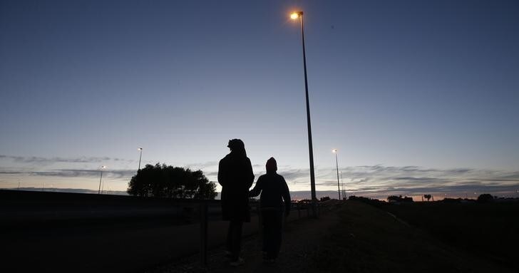 An Eritrean mother and her daughter are seen in silhouette as they walk along the motorway near the Channel Tunnel entrance near Calais, France, August 6, 2015. For most of the 3,000 inhabitants of the "Jungle", a shanty town on the sand dunes of France's north coast, the climax of each day is the nightly bid to sneak into the undersea tunnel they hope will lead to new life in Britain. REUTERS/Peter Nicholls