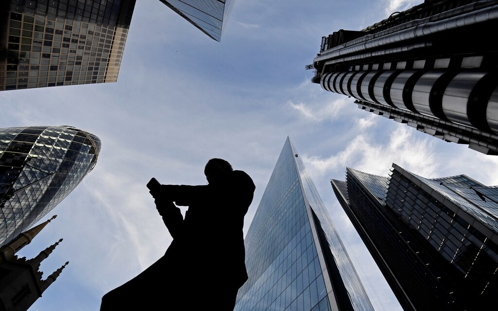 A worker looks at their phone as they walk past The Gherkin, Lloyds, and other office buildings in the City of London, Britain November 13, 2018. REUTERS/Toby Melville - RC1A2B2C9040