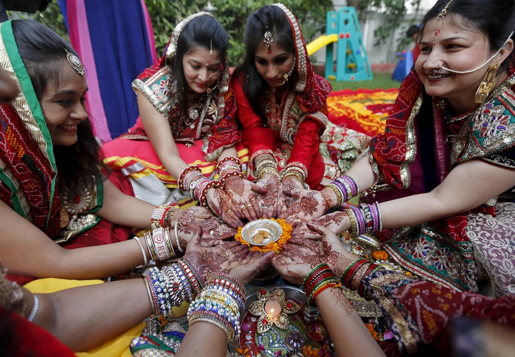 Women with their hands decorated with henna paste pose for pictures as they pray during the Hindu festival of Karva Chauth in Ahmedabad, India, October 30, 2015. Married Hindu women observe a one-day fast and offer prayers for the well-being of their husbands during the festival. The fast begins before sunrise and ends after they worship the moon in the evening. REUTERS/Amit Dave - RTX1TYZU