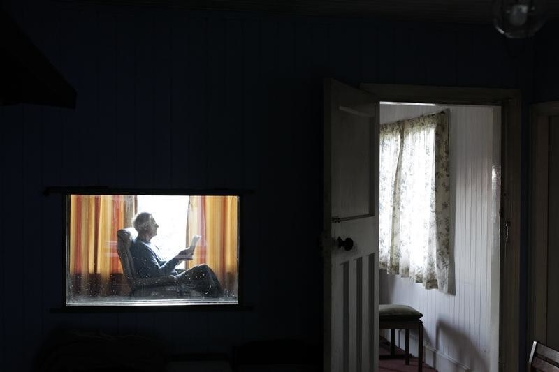John McCarter reads the newspaper by the window in the front living room of his wooden house in the hamlet of Downhill on the north coast of county Londonderry November 22, 2011. McCarter, age 77, has been living without electricity or central heating for the past 29 years. REUTERS/Cathal McNaughton (NORTHERN IRELAND - Tags: SOCIETY) - LM1E7BM15ZX01