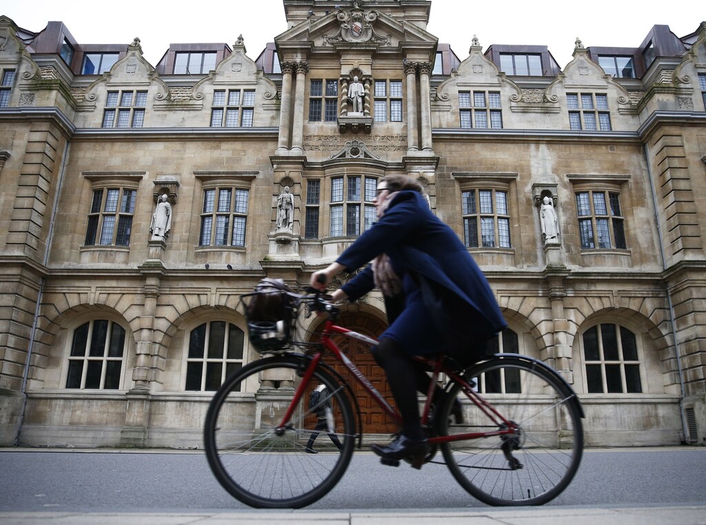 A woman rides a bike next to the Oriel College building with the statue of Cecil Rhodes on its facade in Oxford, southern England, December 30, 2015. REUTERS/Eddie Keogh/File Photo - RTSOWM6