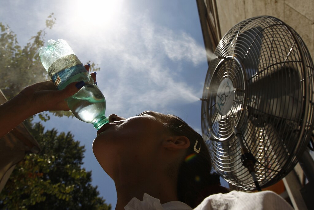 A girl drinks a bottle of water next to a fan spraying water mist on a hot summer day in Rome July 16, 2010. REUTERS/Alessandro Bianchi (ITALY - Tags: ENVIRONMENT SOCIETY) - RTR2GGW7