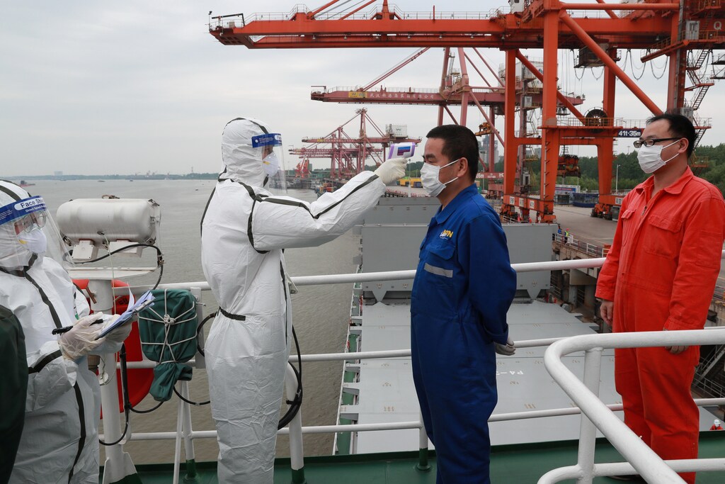 A staff member in protective suit takes body temperature measurement of a crew worker of a cargo ship bound for Japan following the coronavirus disease (COVID-19) outbreak, at a container terminal at a port in Wuhan, Hubei province, China May 9, 2020. Picture taken May 9, 2020. China Daily via REUTERS ATTENTION EDITORS - THIS IMAGE WAS PROVIDED BY A THIRD PARTY. CHINA OUT. - RC2RMG98X0K3