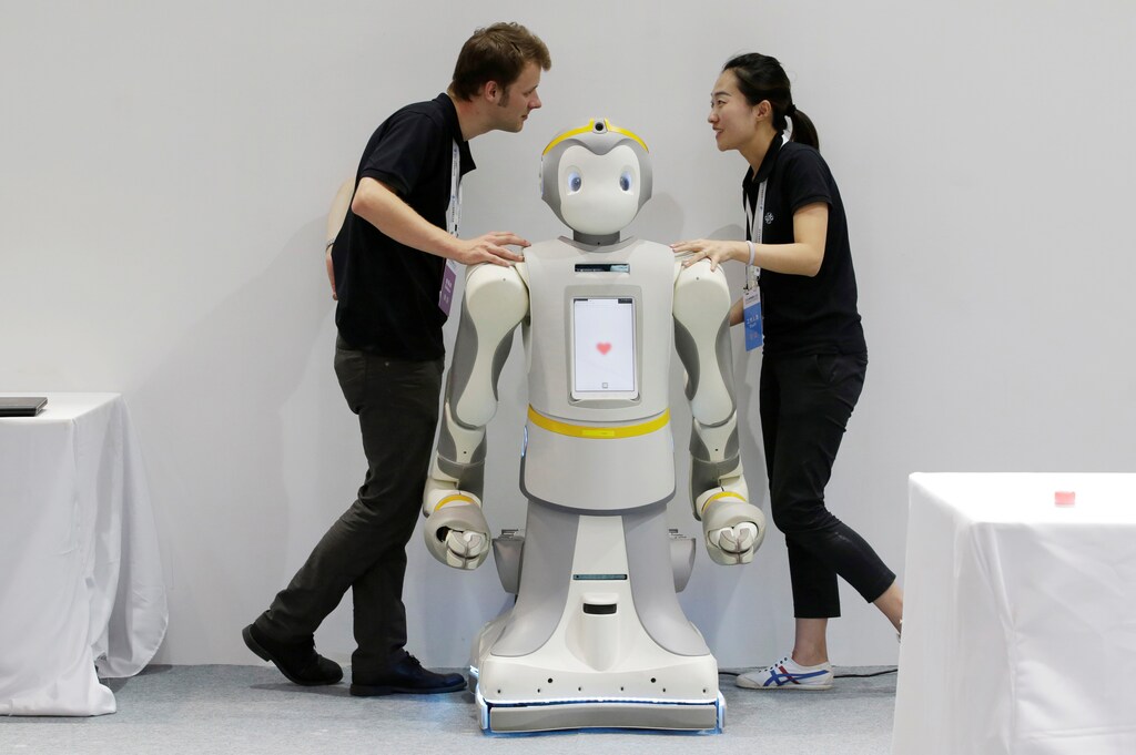 Staff chat next to a P-Care robot at the World Robot Conference (WRC) in Beijing, China August 15, 2018. REUTERS/Jason Lee