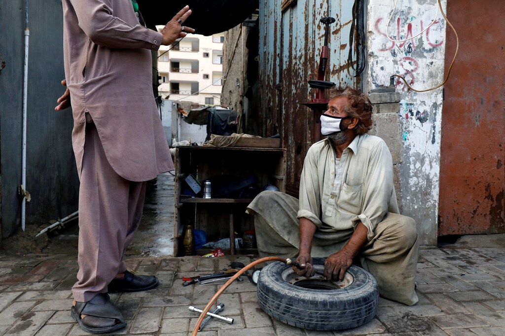 A labourer wearing protective face mask fills air in a tyre at a workshop along a road.