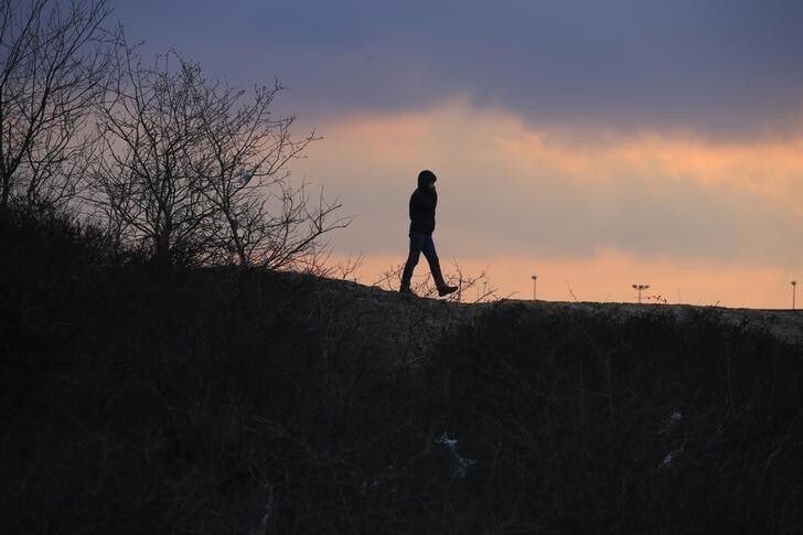 A migrant walks on top of a pile of sand which separates the road that leads to the ferry terminal and the camp known as the "Jungle", a squalid, sprawling camp in Calais, northern France, February 25, 2016. A French judge on Thursday upheld a government plan to partially demolish a shanty town for migrants trying to reach Britain on the outskirts of the northern port of Calais, an official spokesman said. REUTERS/Pascal Rossignol