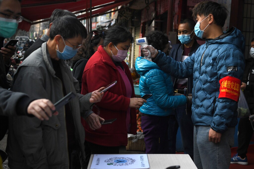 People wearing face masks scan a QR code to submit their personal information while security volunteers check their temperatures at an entrance of a grocery market, as the country is hit by an outbreak of the novel coronavirus, in Kunming, Yunnan province, China February 24, 2020. REUTERS/Stringer CHINA OUT. - RC268F9T0QX1
