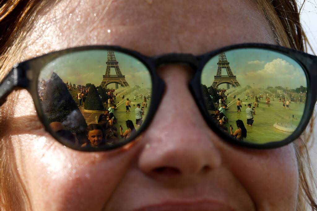 People cooling off in the Trocadero fountains across from the Eiffel Tower are reflected in sunglasses in Paris as a new heatwave broke temperature records in France