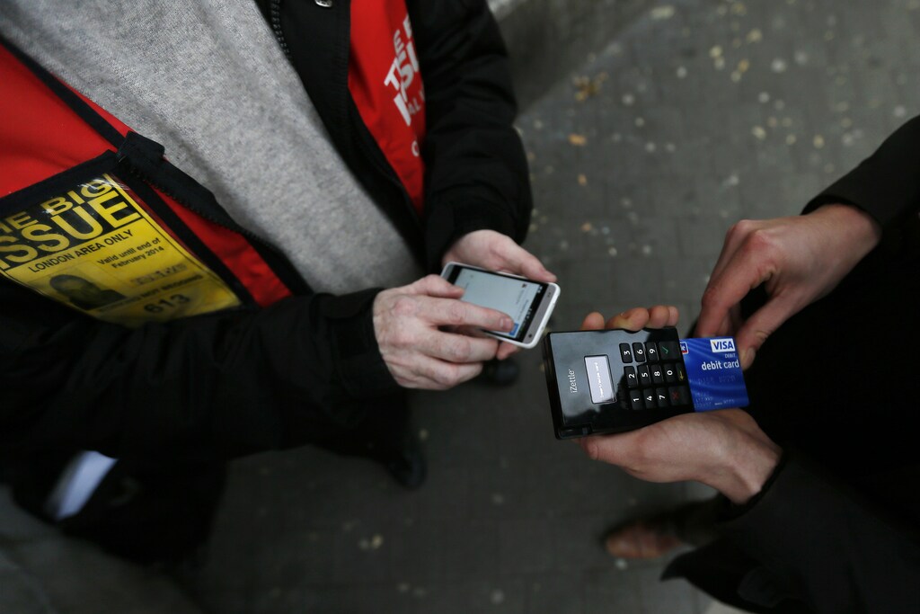 Big Issue vendor Simon Mott (L) demonstrates using his Chip and Pin device outside South Kensington Tube Station in London November 28, 2013. Mott, who sells the Big Issue, a magazine which supports the homeless, has become the first of its vendors to start accepting card payments for the 2.50-pound publication. In an increasingly cashless society, Mott realised that he was losing customers who found themselves without any change, so in May he invested in a card payment system. REUTERS/Stefan Wermuth (BRITAIN - Tags: BUSINESS SOCIETY) - GM1E9BT10LW01