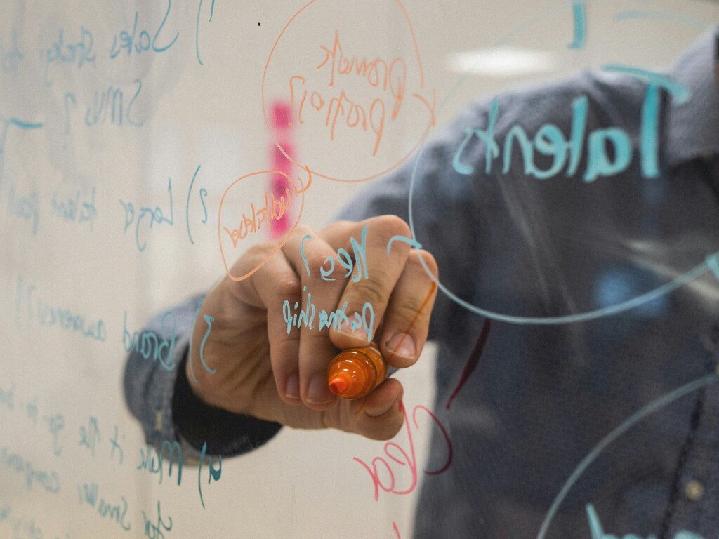 A professional writes strategic notes on a glass board, outlining ideas shaped by data, compliance, and evolving regulation in a business environment.