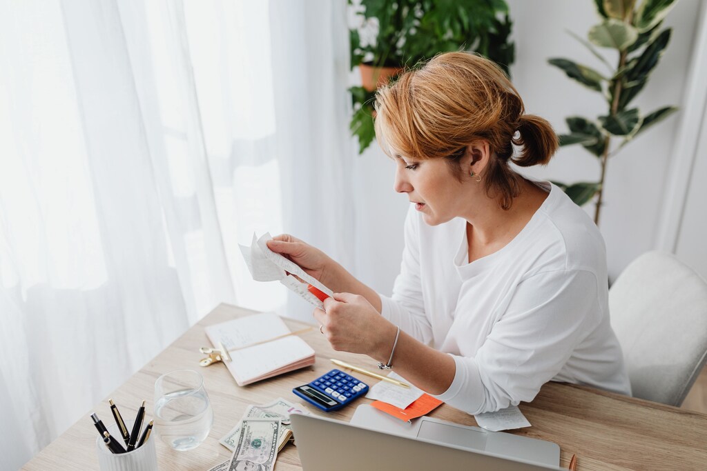 Una mujer con una calculadora sobre el escritorio chequeando una cuenta domestica.