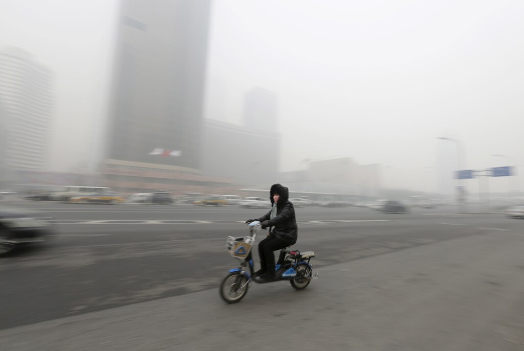 A woman wearing a mask cycles amid heavy smog in Beijing's Guomao area, China, November 30, 2015. REUTERS/Jason Lee