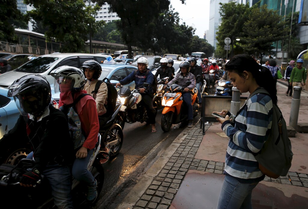 A worker uses her smartphone while waiting for the public bus at a business district street in Jakarta, June 9, 2015. Jakarta's traffic jams are a constant vexation for the city's 10 million residents. With the chaos not looking to abate anytime soon, entrepreneurial types have made it their business to help fellow commuters circumvent the world's worst gridlock. Picture taken June 9, 2015. REUTERS/Beawiharta - RTX1G0NK