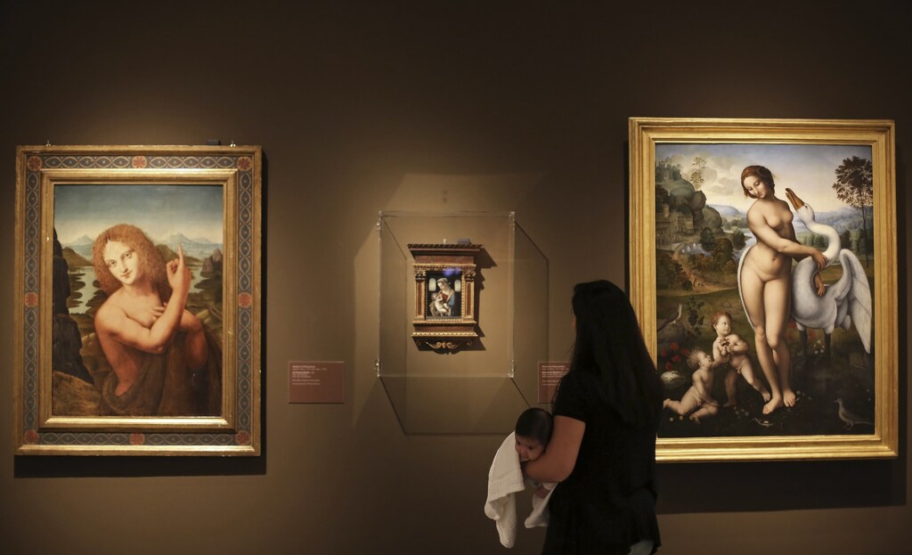 A visitor carrying her baby looks at the "San John the Baptist" (L) and the "Madonna with Child", paintings by artist Marco D'Oggiono, and "Leda and the Swan" (R), a painting by artist Leonardo Da Vinci, during the "Masters of the Renaissance, Masterpieces from Italy" exhibition at the Bank of Brazil Cultural Centre in Sao Paulo July 13, 2013. The exhibition will run from July 13 to September 23. REUTERS/Nacho Doce (BRAZIL - Tags: SOCIETY) - GM1E97E0IME01
