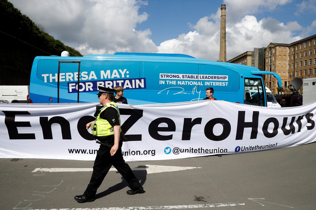A police officer walks in front of a banner protesting against zero hours contracts in Halifax, United Kingdom.