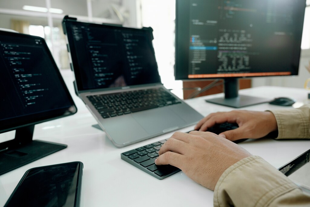 Cybersecurity professional monitoring code and system data across multiple computer screens at a workstation.