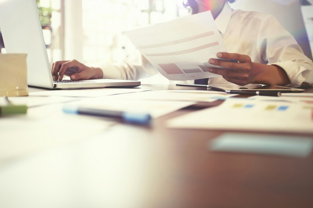 Someone in a white shirt looks at papers while tapping on a laptop: Stress intelligence is becoming an essential and strategic leadership capability