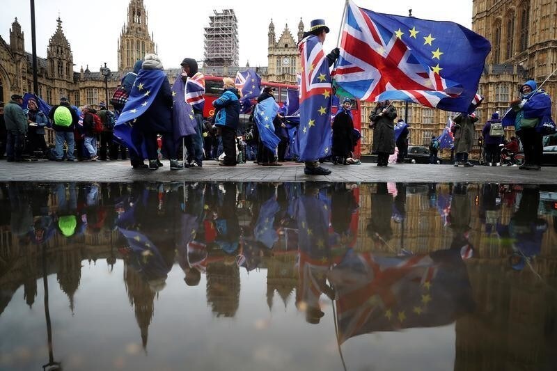 Anti-Brexit protesters are reflected in a puddle as they demonstrate opposite the Houses of Parliament in London, Britain, April 30, 2018.