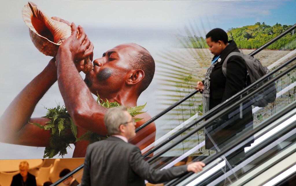 People pass by a placard prior to the COP23 UN Climate Change Conference 2017, hosted by Fiji but held in Bonn, in World Conference Center Bonn, Germany, November 6, 2017. REUTERS/Wolfgang Rattay - RC116042C590