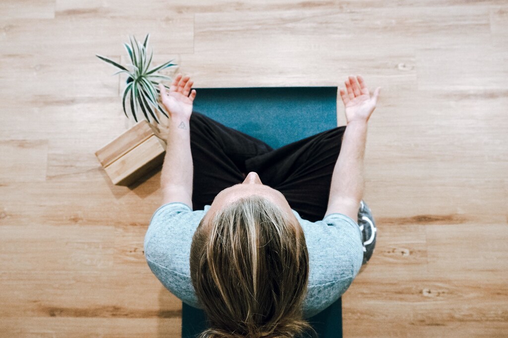 Person in grey shirt and black trousers sitting on a wooden floor: Meditation can help people feel calm, relaxed and mentally balanced.
