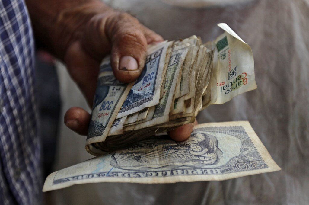 A farmer holds a wad of Cuban money at a vegetable stall at a market in Sagua La Grande, in the province of Villaclara in central Cuba, around 240 km (149 miles) east of Havana October 12, 2013. Cuba took the first step towards scrapping its two-tier currency on October 22, 2013, in a move which could boost local workers' income and remove a major hurdle for importers and exporters. Cuba's convertible peso (CUC) is pegged to the U.S. dollar, while the local peso (CUP) is valued at a fraction of the greenback's value, angering the population which is paid in the latter, and complicating accounting, the evaluation of performance, and trade for state companies. Picture taken October 12, 2013. REUTERS/Desmond Boylan (CUBA - Tags: SOCIETY BUSINESS AGRICULTURE) - GM1E9AN0M3801