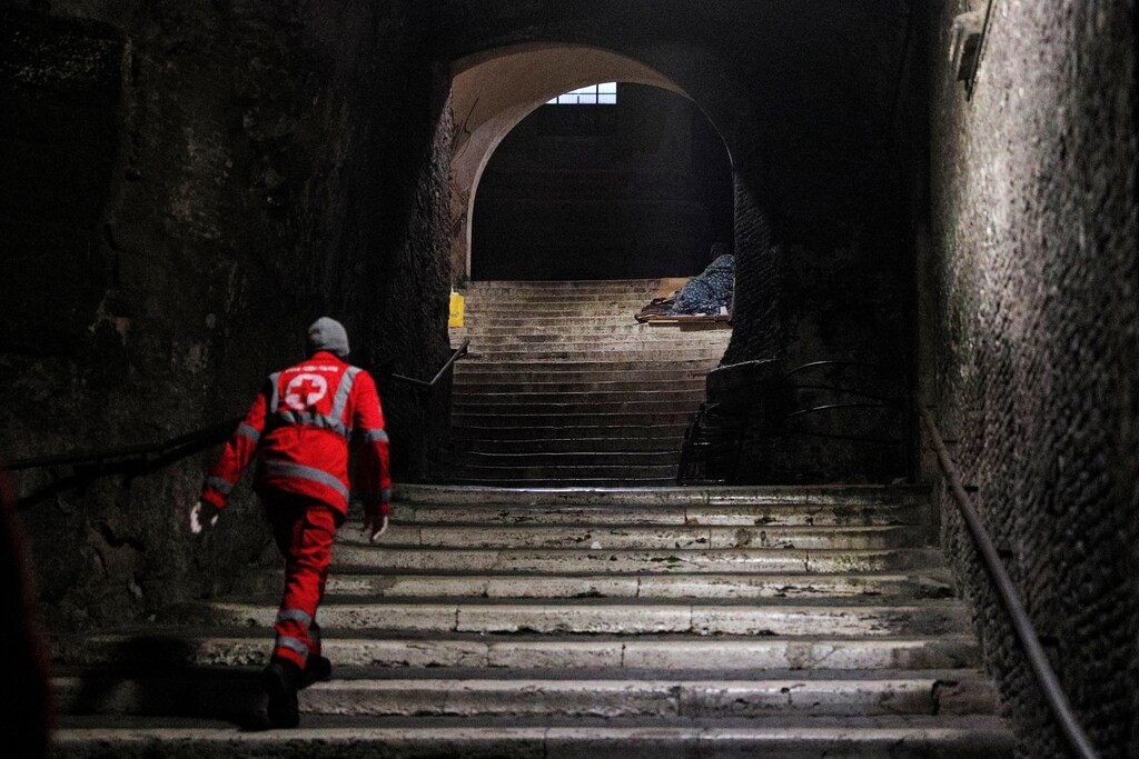 Un trabajador de la Cruz Roja revisa a un indigente acostado en un escalón cerca del Coliseo en Roma, Italia, el 17 de marzo de 2020.