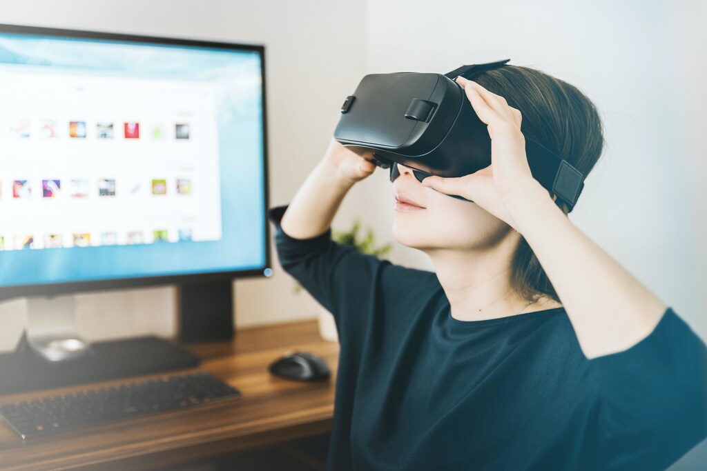 A woman wearing a virtual reality (VR) headset, with a computer in the background.