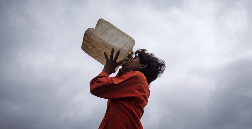 A boy drinks water from a jerry can against the backdrop of monsoon clouds early morning in Karachi July 25, 2012. REUTERS/Akhtar Soomro (PAKISTAN - Tags: SOCIETY ENVIRONMENT BUSINESS EMPLOYMENT POVERTY) - GM1E87P1A7A01