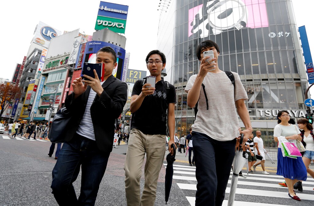 Men play the augmented reality mobile game "Pokemon Go" by Nintendo on their mobile phone as they walk at a busy crossing in Shibuya district in Tokyo, Japan, July 22, 2016.