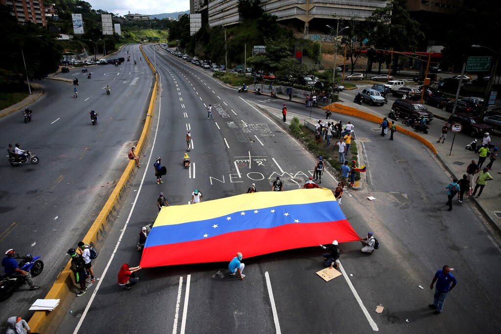Demonstrators hold a Venezuelan flag as they block a main street during protests against Venezuela's president Nicolas Maduro government in Caracas, Venezuela, June 12, 2017. REUTERS/Ivan Alvarado - RTS16SAA
