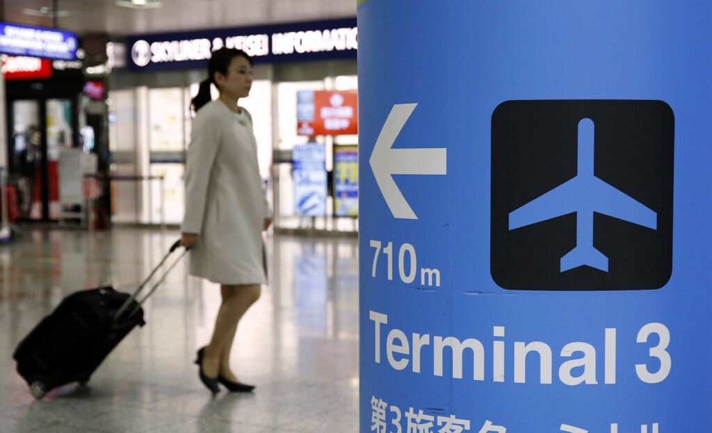 A woman is seen behind a sign indicating the direction to terminal 3 at Narita International airport terminal 2 in Narita, near Tokyo, Japan, March 25, 2016.