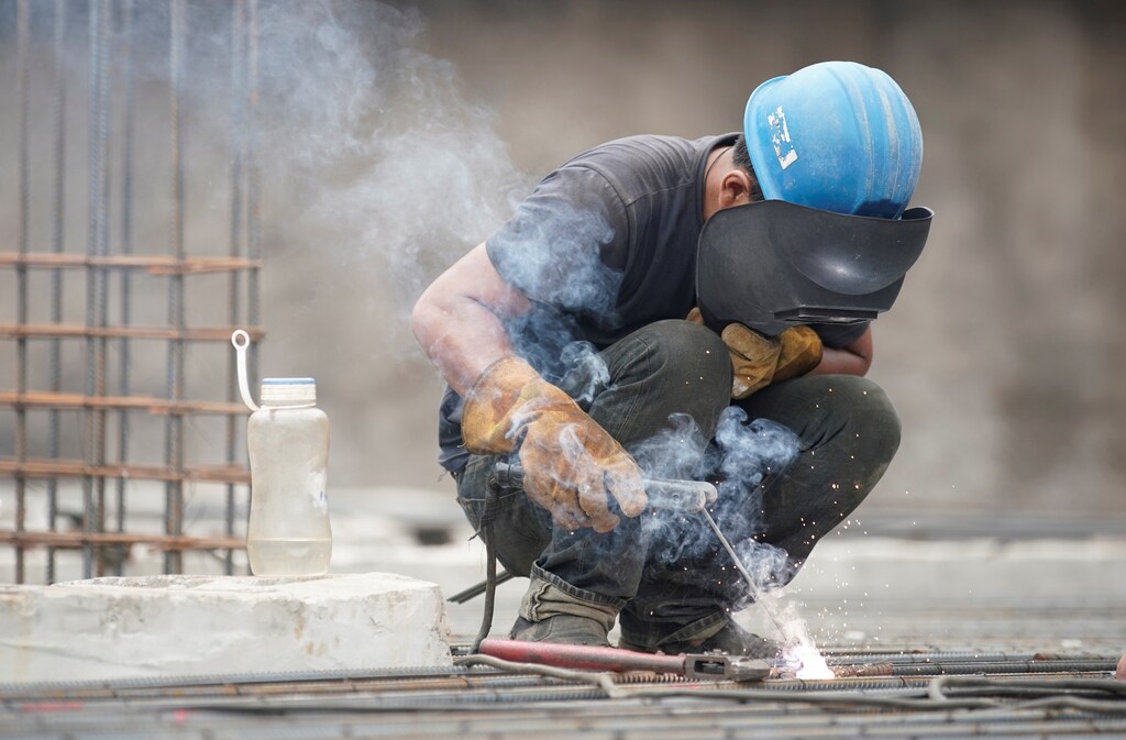 A migrant worker welds metal at a construction site.