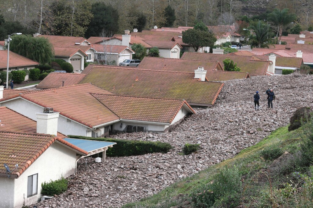 A TV news crew files a report behind damaged homes after a mud slide overtook at least 18 homes during heavy rains in Camarillo Springs, California December 12, 2014. A major storm pummeled California and the Pacific Northwest with heavy rain and high winds on Thursday, killing one man, knocking out power to tens of thousands of homes, disrupting flights and prompting schools to close.