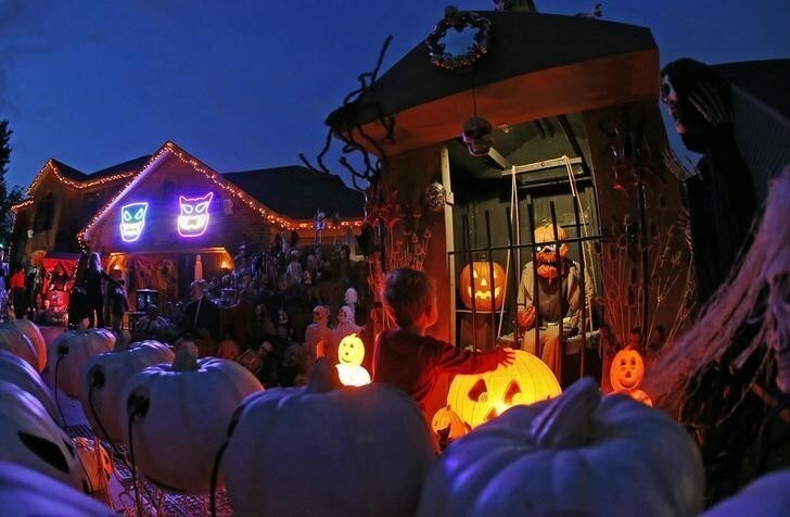 A visitor to a house covered in Halloween decorations looks over the scene in the front yard in the Chicago suburb of Naperville, Illinois, October 27, 2014. Breathtaking purple-and-orange light displays, zombie graveyards, mutilated mannequins and singing inflatable pumpkins are just some of the front-yard Halloween decorations that Americans are expected to spend $7.4 billion on this year. In the Chicago suburb of Naperville, the displays got so elaborate that Annette Wehrli decided to set up a tour. Wehrli's Naperville Trolley & Tours, which has run tours of Christmas lights for 19 years, put Halloween on the schedule at the suggestion of enthusiastic residents of the sprawling upper middle-class city of 200,000. Picture taken October, 27, 2014.REUTERS/Jim Young (UNITED STATES - Tags: SOCIETY TPX IMAGES OF THE DAY)
