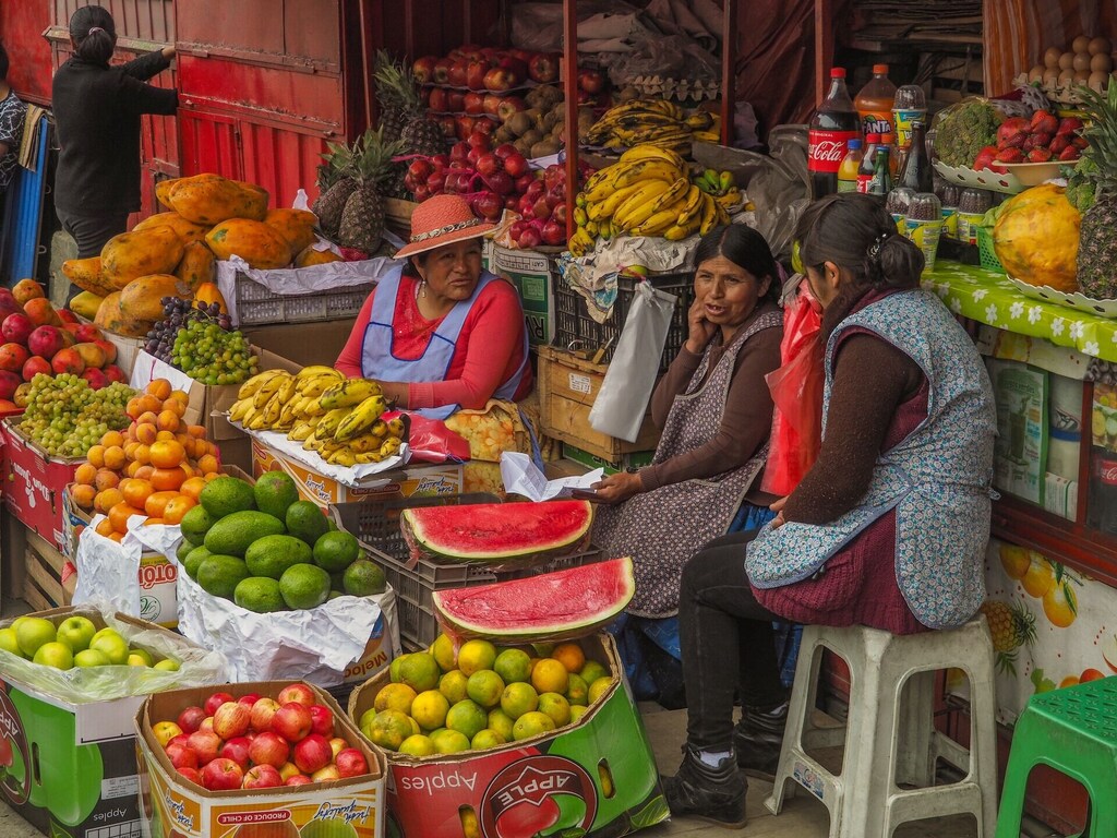 Tres mujeres sentadas con frutas diversas en un mercado en Bolivia.