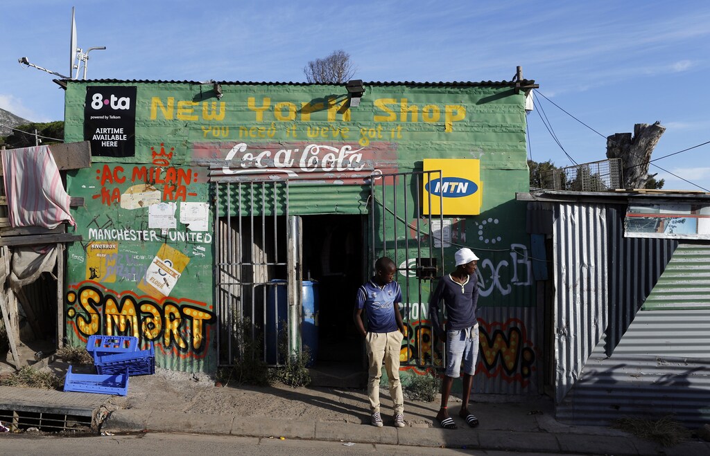 Residents stand outside a spaza convienience shop in Cape Town's Imizamo Yethu township, April 19, 2014. Along with shebeens, or corner taverns, spazas are one of the most visible parts of township life, and a major component of South Africa's vast informal economy. While recent data on the informal economy is hard to come by, a 2002 study by the University of South Africa's Bureau of Market Research estimated that spaza shops brought in around $705 million a year, employing up to 290,000 people. Those numbers will have come under pressure over the last decade as real estate developers and big grocers such as Shoprite and Pick N Pay push into black areas, targeting rising consumer spending. Picture taken April 19. REUTERS/Mike Hutchings (SOUTH AFRICA - Tags: BUSINESS SOCIETY)