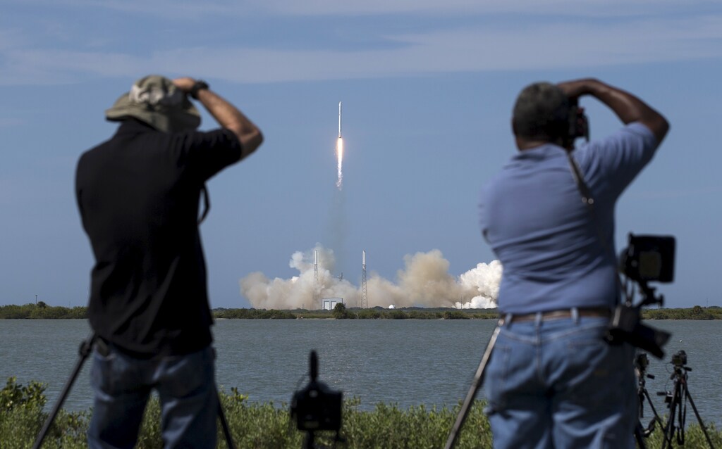 Photographers take pictures of the unmanned SpaceX rocket as it launches from Cape Canaveral, Florida