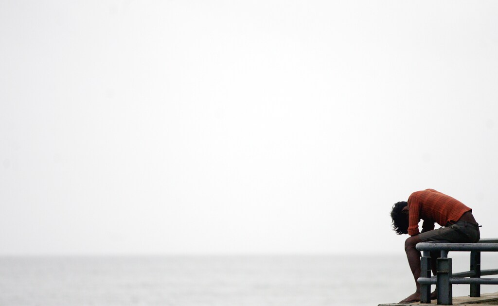 An Indian man sits near a beach in Bombay August 4, 2005. India will be hit by billions of dollars in losses because of last week's heavy rains and floods in the west, and many already-impoverished people will be wiped out financially, insurers and aid workers said on Wednesday. The state government's initial response has come under fire from aid agencies, who say it is still not doing enough to help the most desperate people. REUTERS/Arko Datta AD/NL - RP6DRMTUOEAA